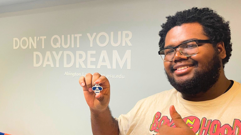 Darryl Gregory holds up a 3D print of a bee in front of a wall that says "Don't quit your daydream."