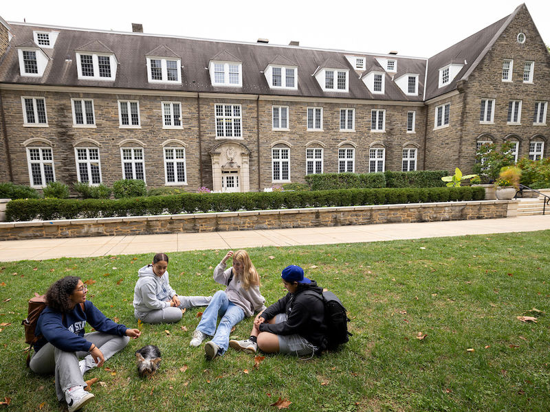 four students sitting on the grass in front of Sutherland building