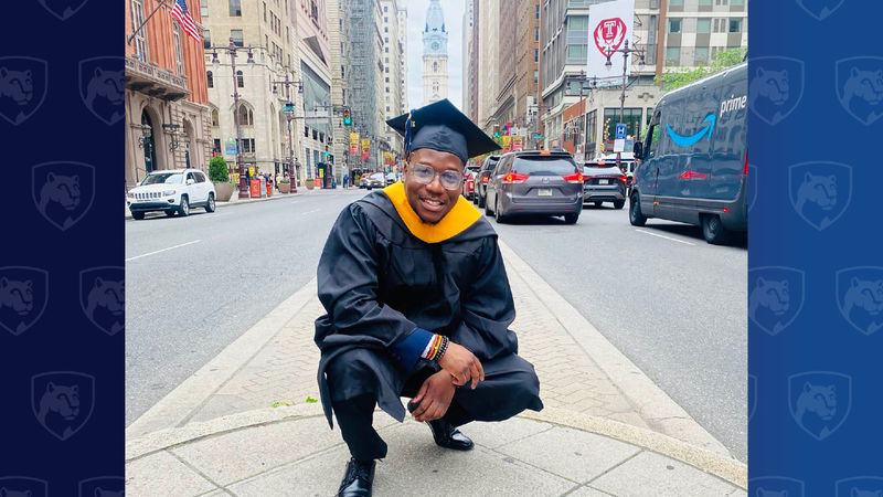 Man in cap and gown crouching near City Hall in Philadelphia