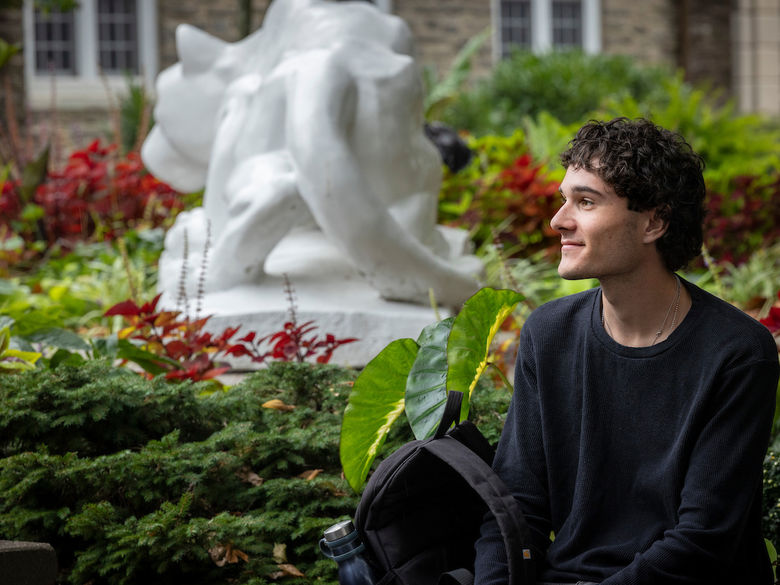 student gazing off into the distance with lion shrine behind him