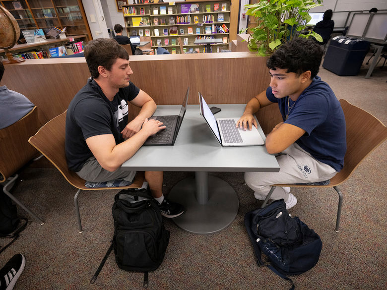 two students with their laptops at a table in the library