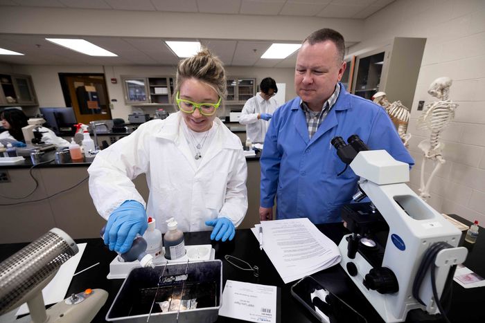 student in lab coat working with their professor