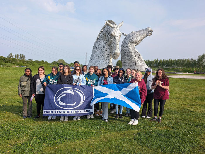 Students with a flag in front of twin horse statues