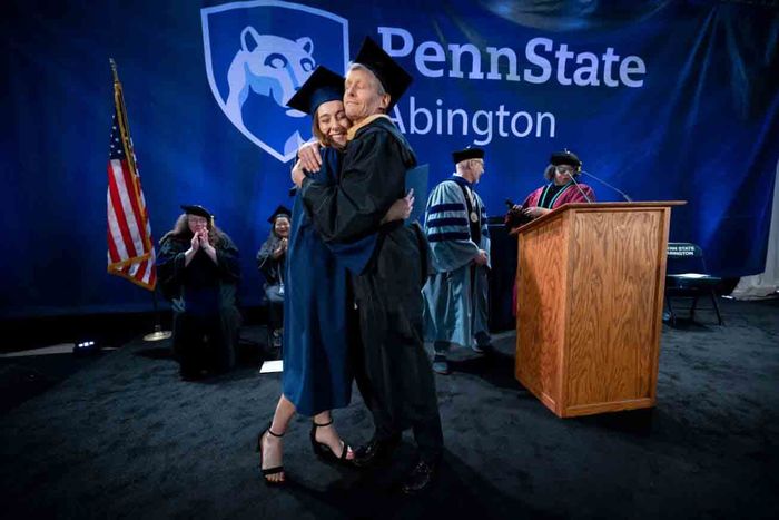 student and professor hugging on commencement stage