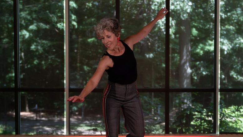 Woman tap dancing in a studio in front of wall of windows