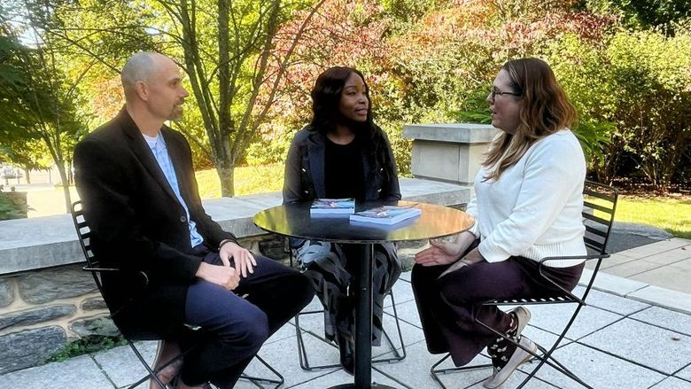 Three people around an outdoor table talking