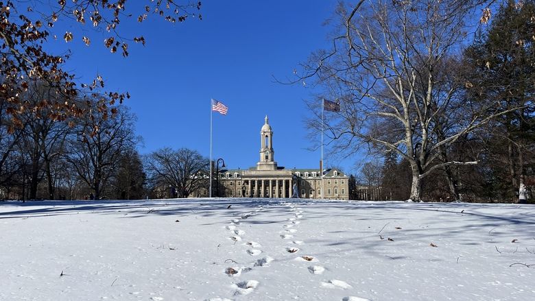 A faraway picture of Old Main with a blue sky behind it and several paths of footprints in the snow leading to it