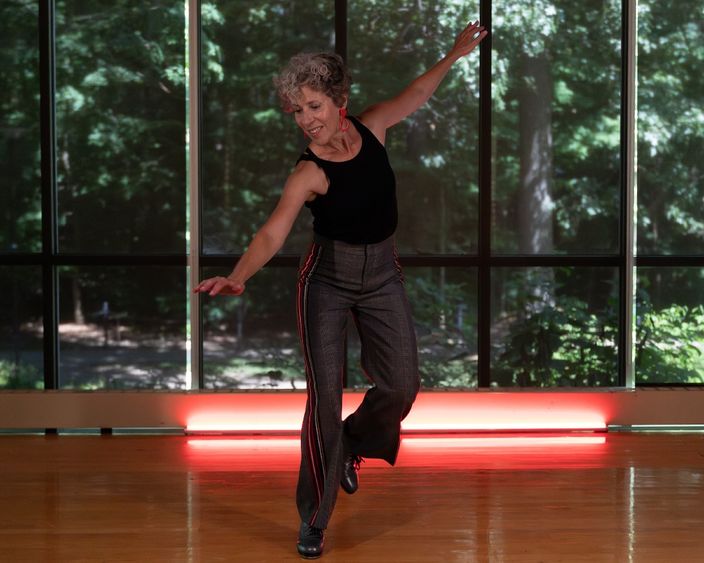 Woman tap dancing in a studio in front of wall of windows