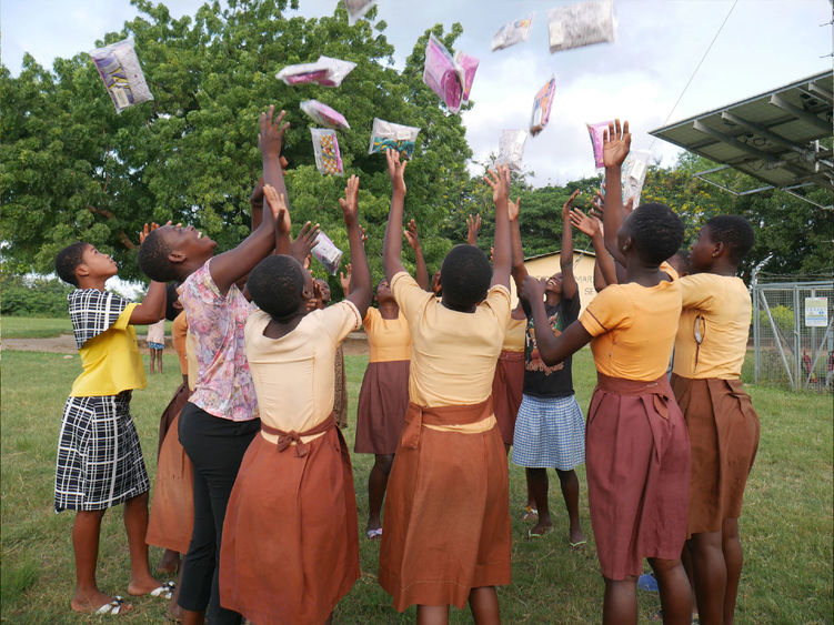 Students in Ghana throw period products in the air